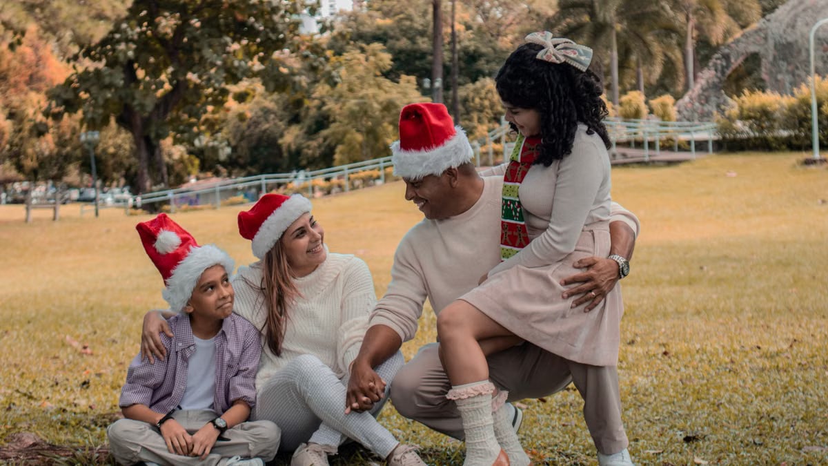 A joyful family wearing Santa hats enjoying Christmas in a sunny park.